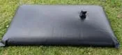 Black flat pillow-style water storage tank on grass, designed for flexible outdoor water storage.