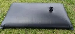 Black flexible water bladder for outdoor water storage on grassy terrain.