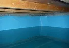 Interior view of a water storage tank showing water levels beneath a wooden frame structure, likely used for potable water storage or rainwater collection.