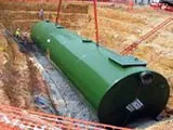 A large green water storage tank being installed underground at a construction site with workers and equipment visible.