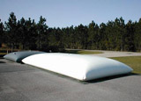 Flat white pillow tanks used for water storage, placed on a paved surface near trees.