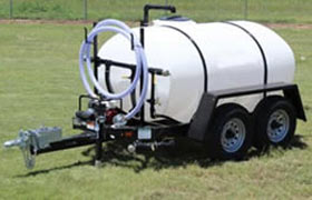 Towable water trailer with a white tank and dual-axle wheels, equipped with hoses for portable water transport.