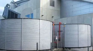 Two large cylindrical corrugated steel tanks with vertical walls, situated near an industrial building.