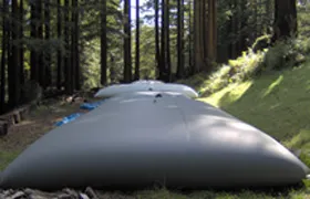 Grey water storage bladder tanks placed in a forested area for environmental or emergency water storage.