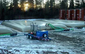 Multiple beige water storage bladder tanks connected with hoses in a snow-covered industrial site.