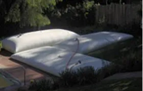 White water storage bladder tanks set up in a residential backyard, likely for irrigation or rainwater collection.