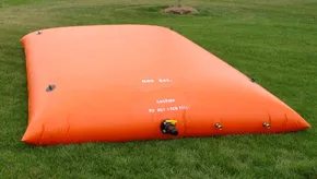 Large orange water storage bladder tank laid on a grassy field, used for potable or non-potable water storage.