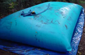 Blue collapsible rainwater storage bladder placed on a tarp outdoors for rainwater harvesting.